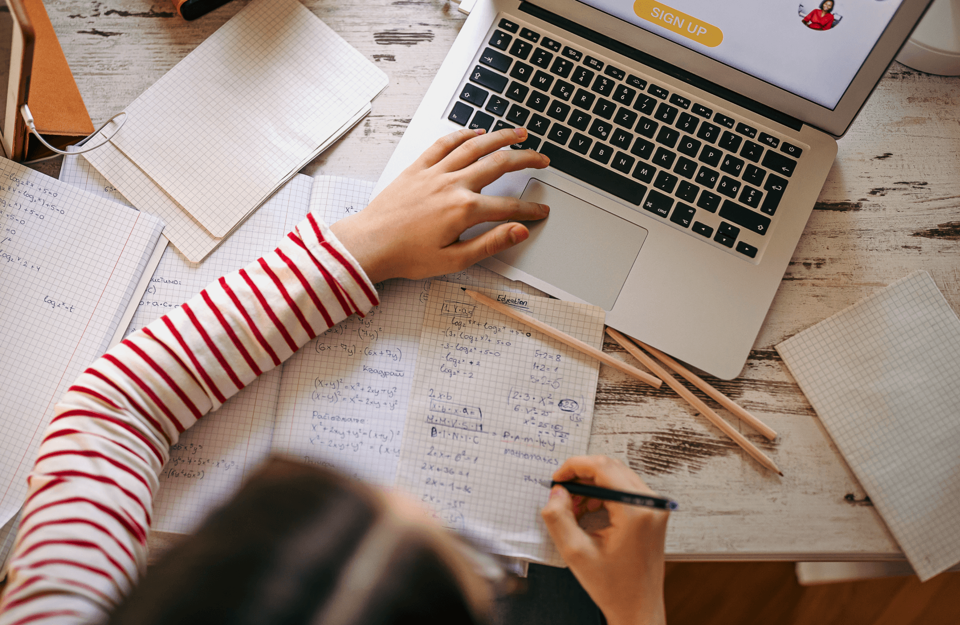 Student writing in a notebook beside an open laptop